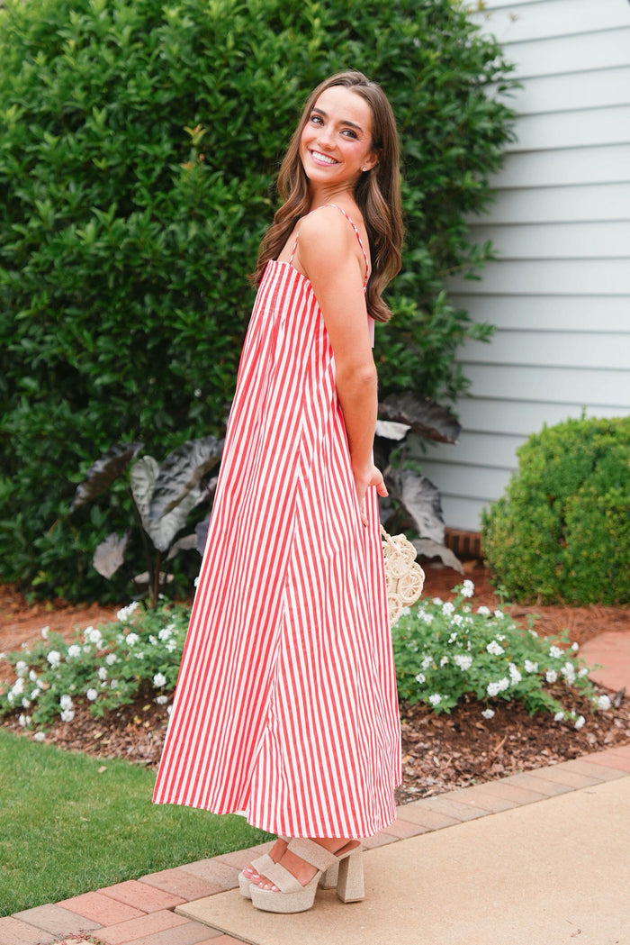 Woman in a red and white striped dress standing outdoors next to a house.