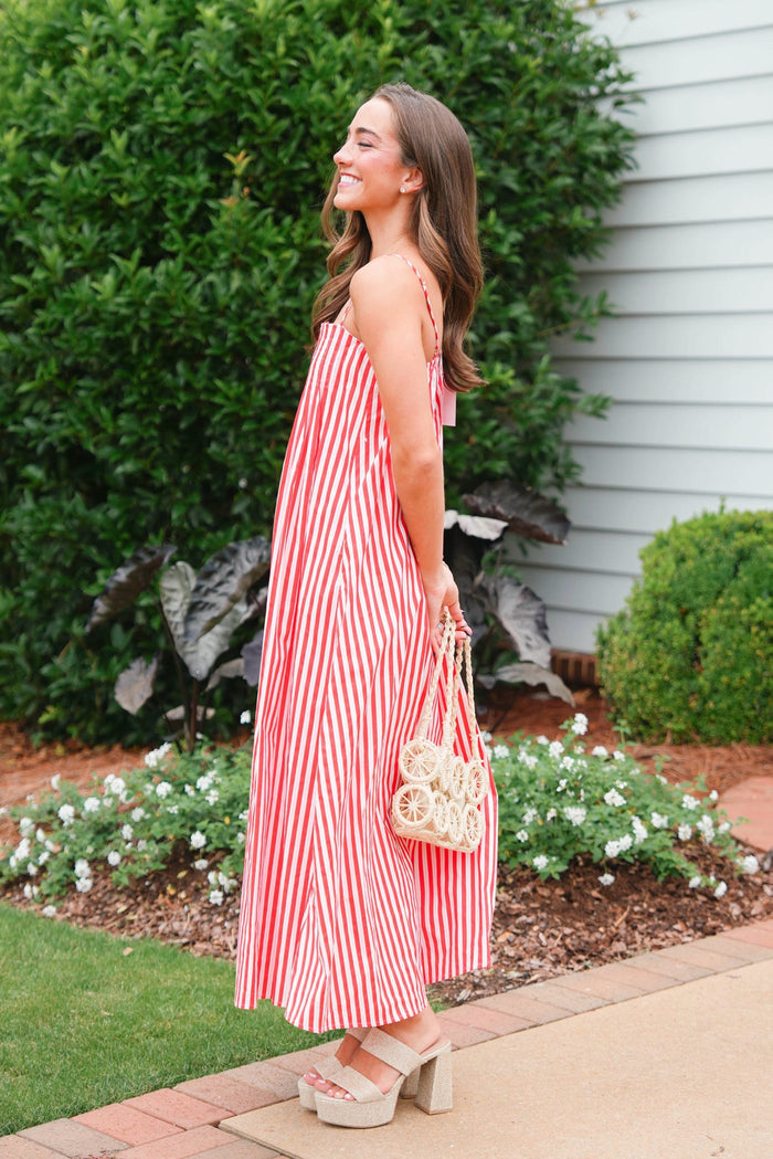 Woman in a red and white striped dress standing outdoors near a garden.