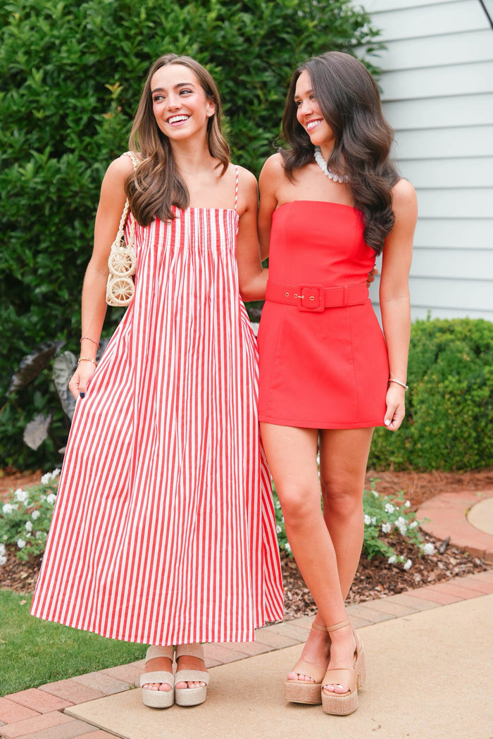 Two women in red and white striped and solid red dresses standing outdoors.
