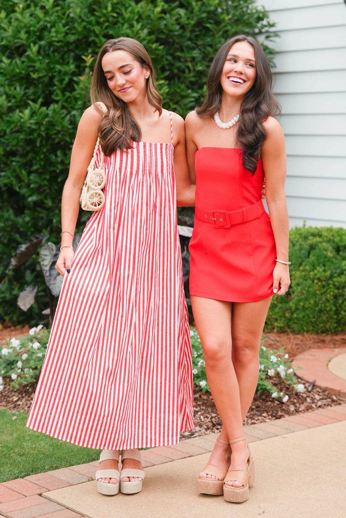 Two women in summer dresses standing outdoors with greenery in the background