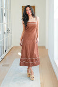 Woman wearing a brown dress with white trim in a room with wooden floor and white walls.