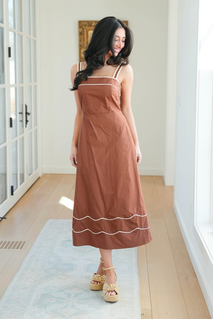 Woman wearing a brown dress with white trim in a bright room.