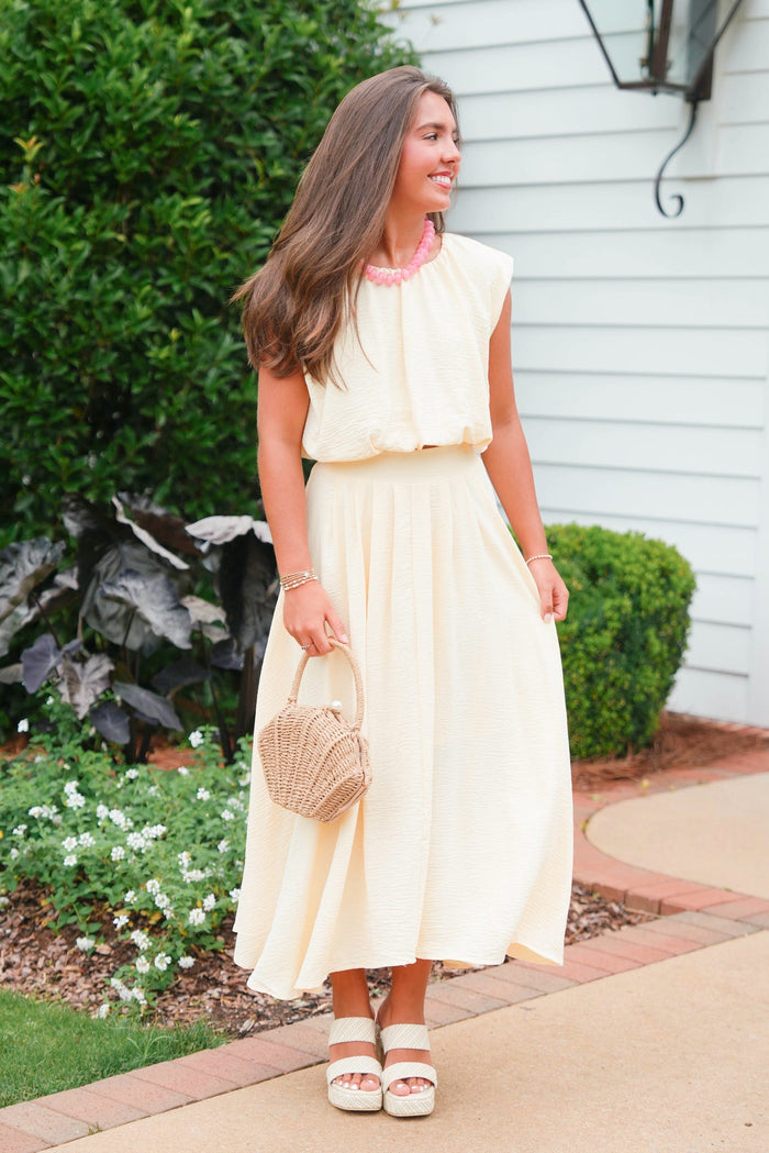Woman in a white dress holding a straw bag outdoors.
