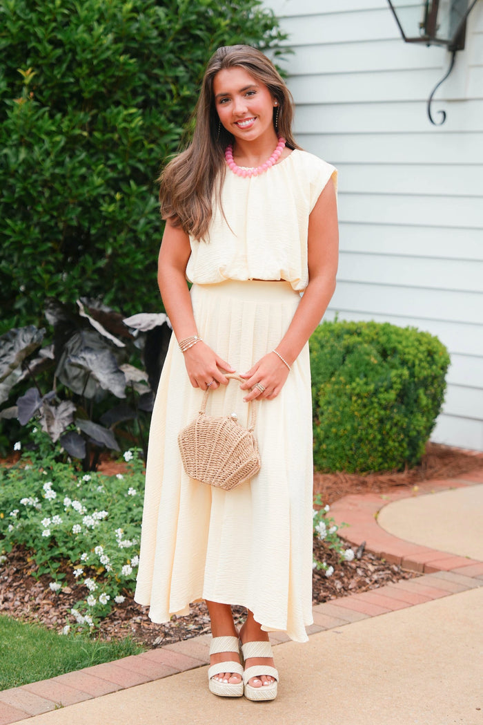 Woman in a white dress standing outdoors with greenery and a house in the background