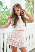 Woman wearing a white lace top and pink floral skirt on a balcony.