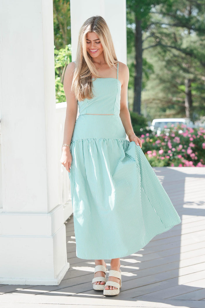 Woman in a light blue dress standing outdoors with greenery and flowers in the background