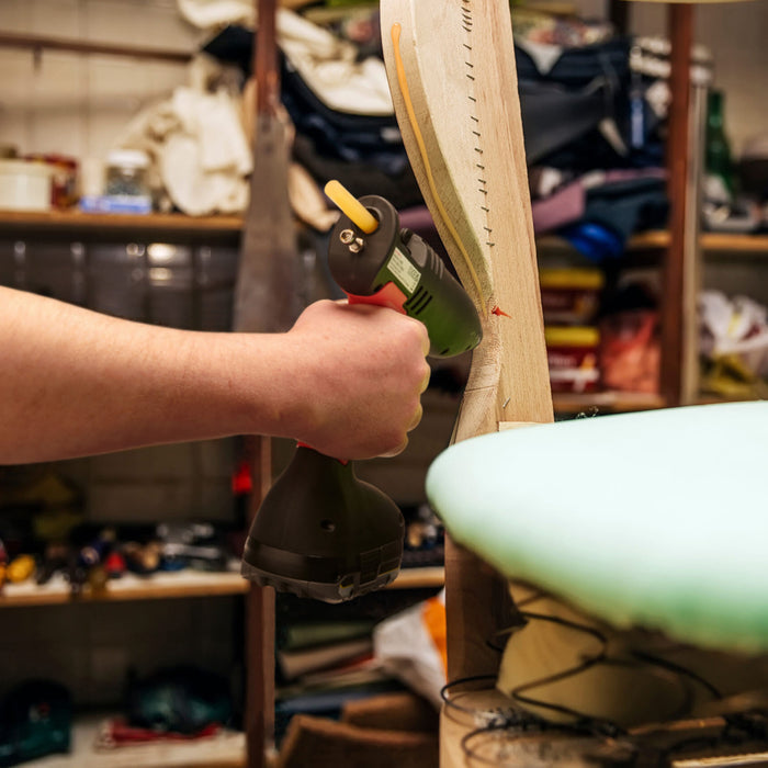 Cordless Tec 808 hot melt glue gun applying adhesive to furniture frame during upholstery work