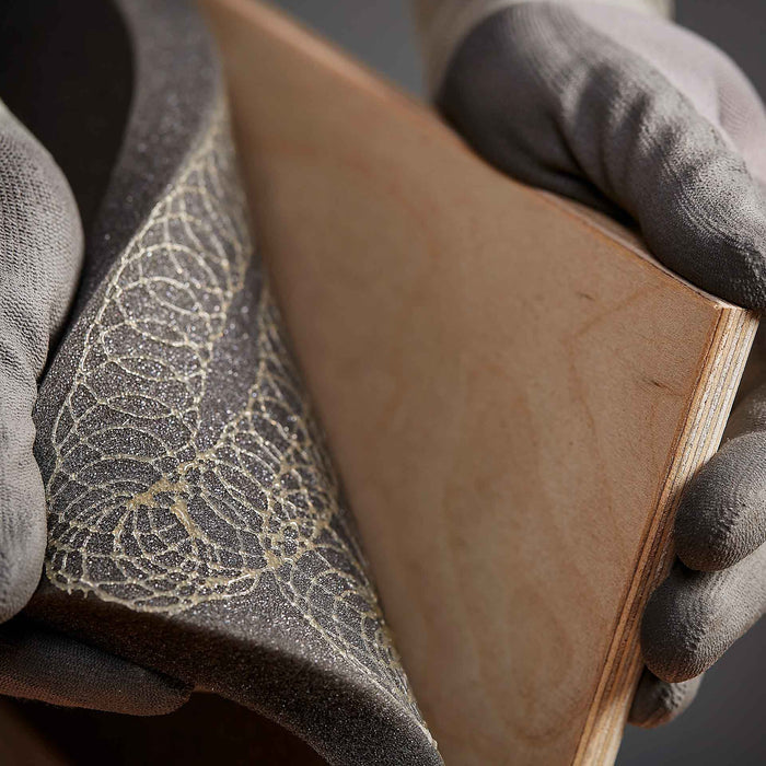 Close-up view of hot melt adhesive sprayed between foam and wood, showing bonded materials after application.