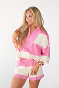 A woman modeling a pink and cream striped knit romper with a half-zip neckline and elbow-length sleeves, photographed against a plain light background.
