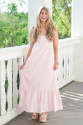 Woman in a pink dress standing on a wooden deck with greenery in the background