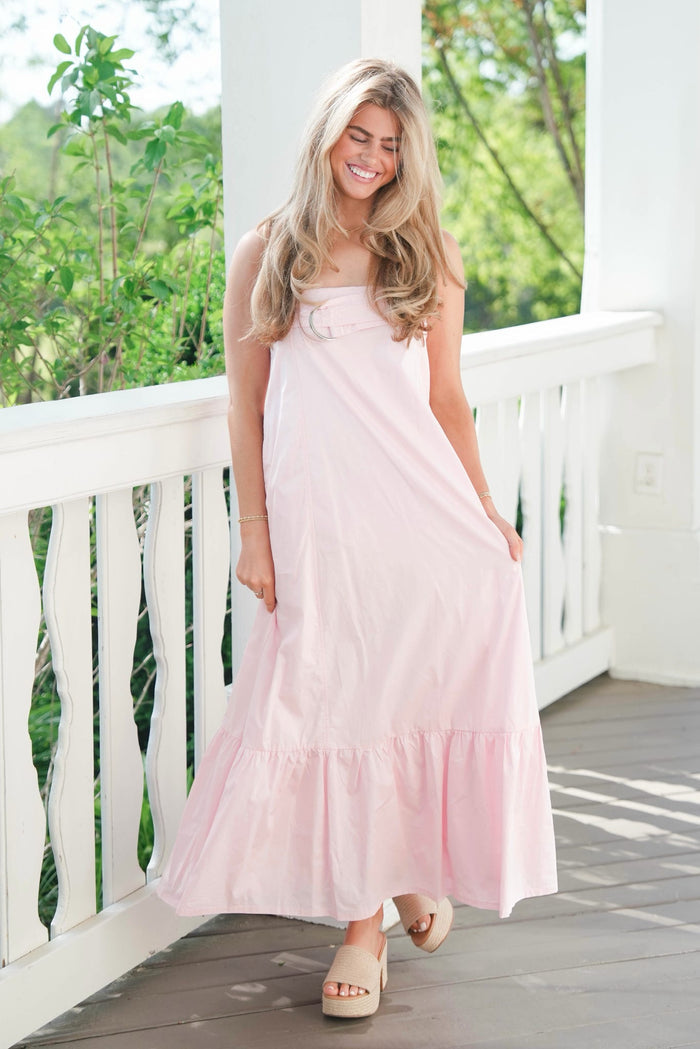 Woman in a pink dress standing on a wooden deck with greenery in the background
