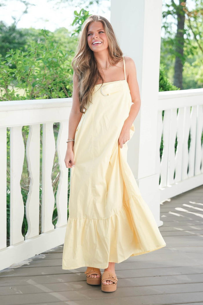 Woman in a yellow dress standing on a wooden deck with white railings.