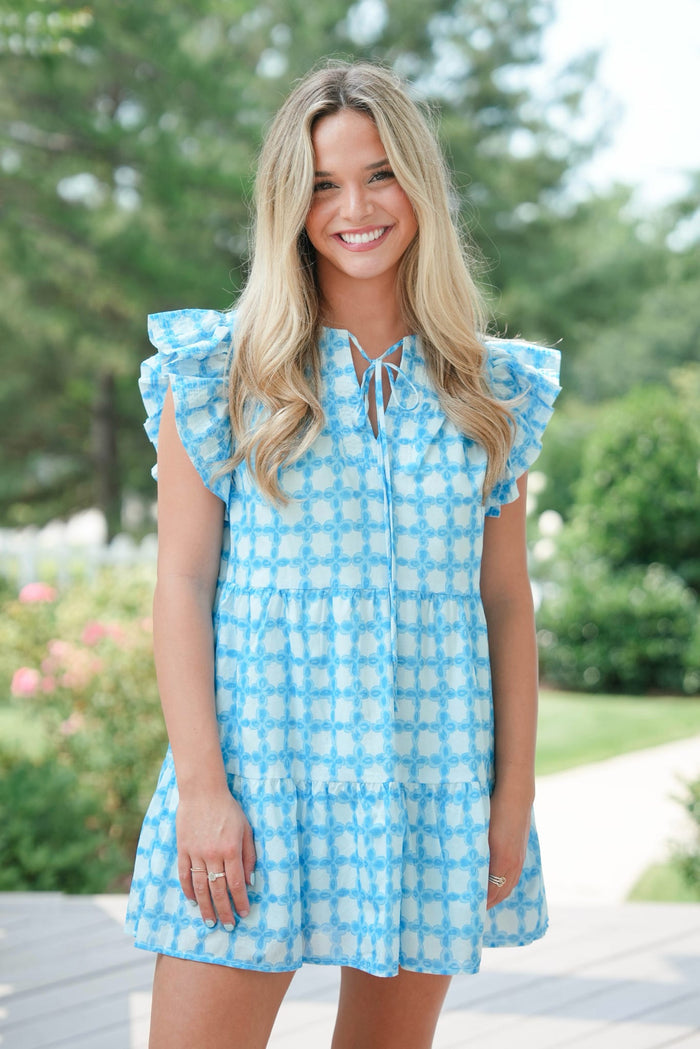 Woman wearing a blue checkered dress standing outdoors with greenery in the background