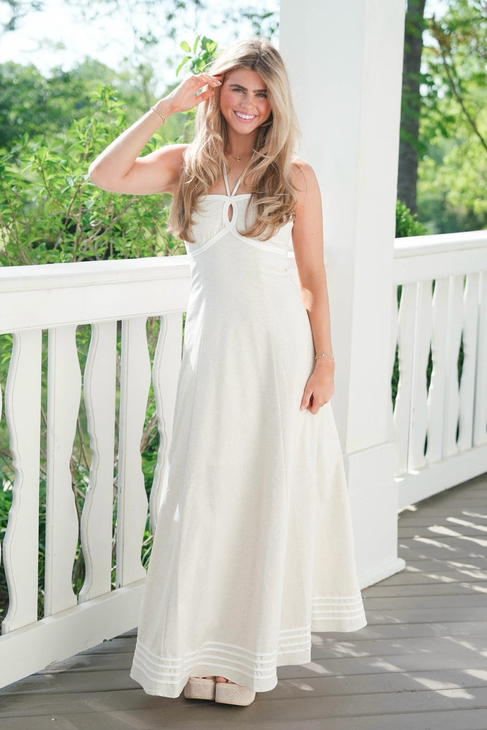 Woman in a white dress standing on a wooden deck with greenery in the background
