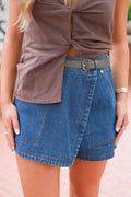 A close-up of a person wearing a brown twisted-front top and a blue denim wrap-style mini skirt with a dark belt and silver buckle.