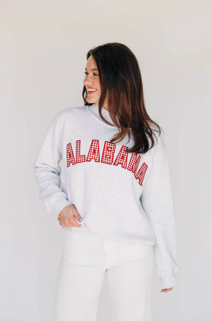 Woman wearing a white sweatshirt with 'Alabama' printed on it against a plain background