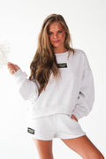 A woman modeling a light gray heather sweatshirt and matching shorts set. The set features a black rectangular chest patch on the sweatshirt and a matching patch on the shorts, both reading 'FASHION FOREVER'.