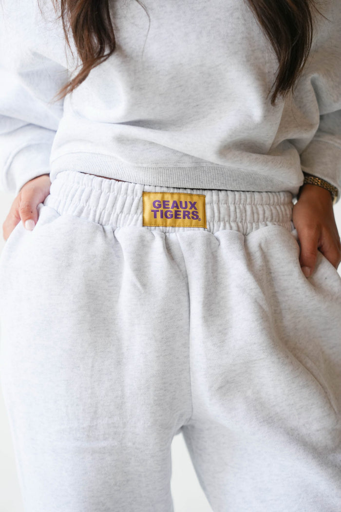Close-up of a person wearing light heather gray sweatpants with a yellow waistband patch reading 'GEAUX TIGERS' and a matching light gray sweatshirt.