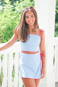 Woman wearing a light blue dress with red accents standing outdoors.