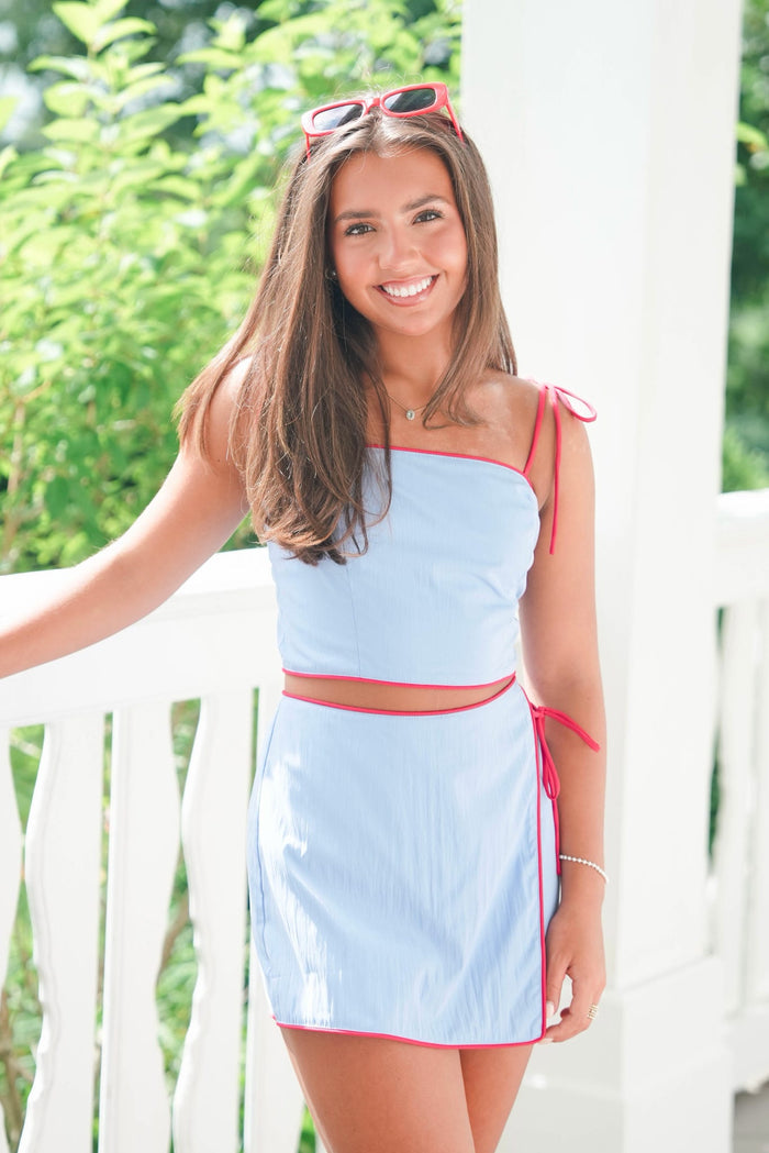 Woman wearing a light blue dress with red accents standing outdoors.
