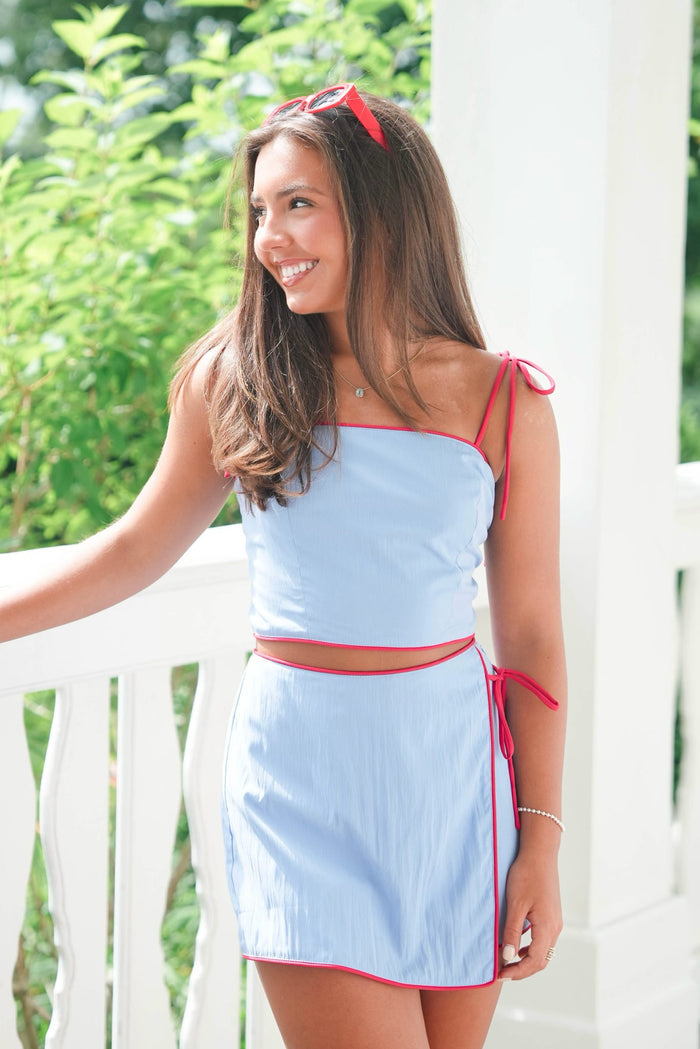 Woman wearing a light blue dress with red accents on a white railing.