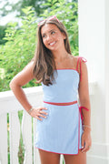 Woman wearing a light blue dress with red accents on a white railing.