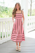 Woman wearing a pink and brown striped dress on a wooden deck.