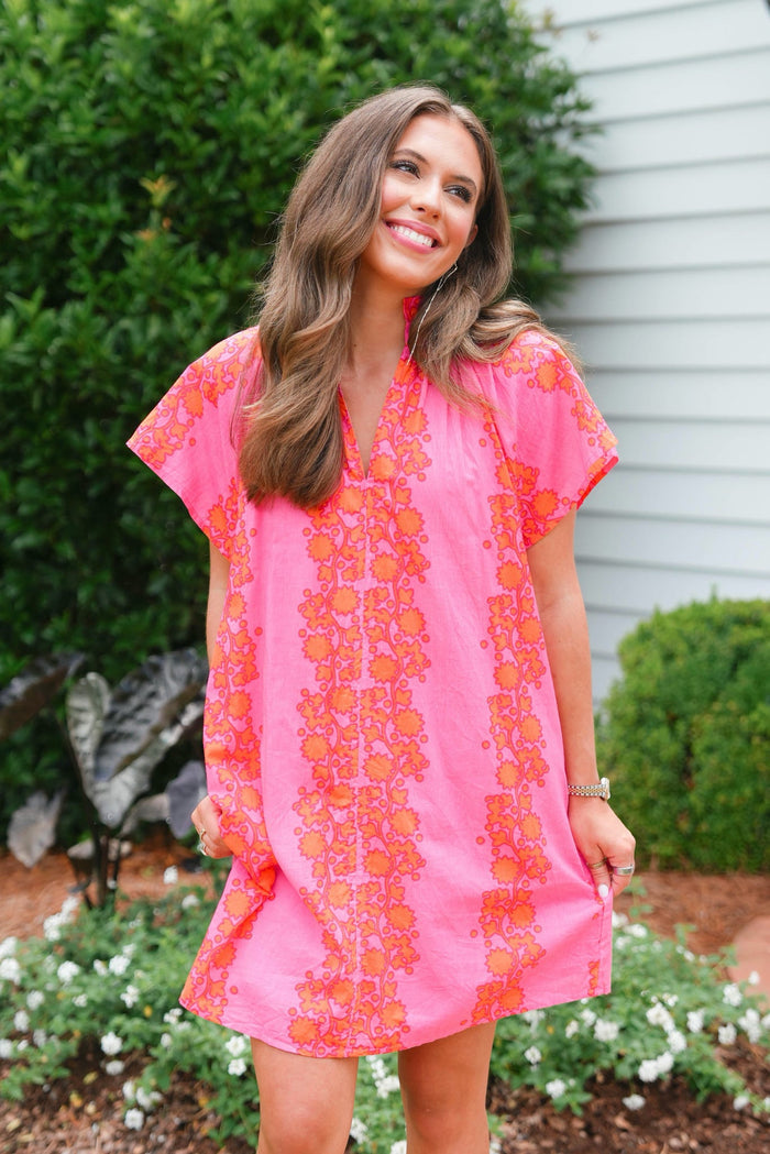 Woman wearing a pink dress with orange floral pattern outdoors.