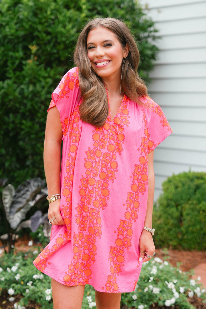 Woman wearing a pink floral dress standing outdoors with greenery in the background