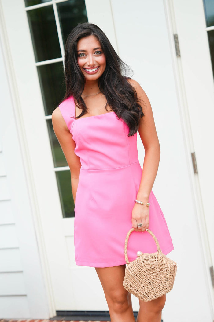 Woman in a pink dress holding a straw bag outdoors.