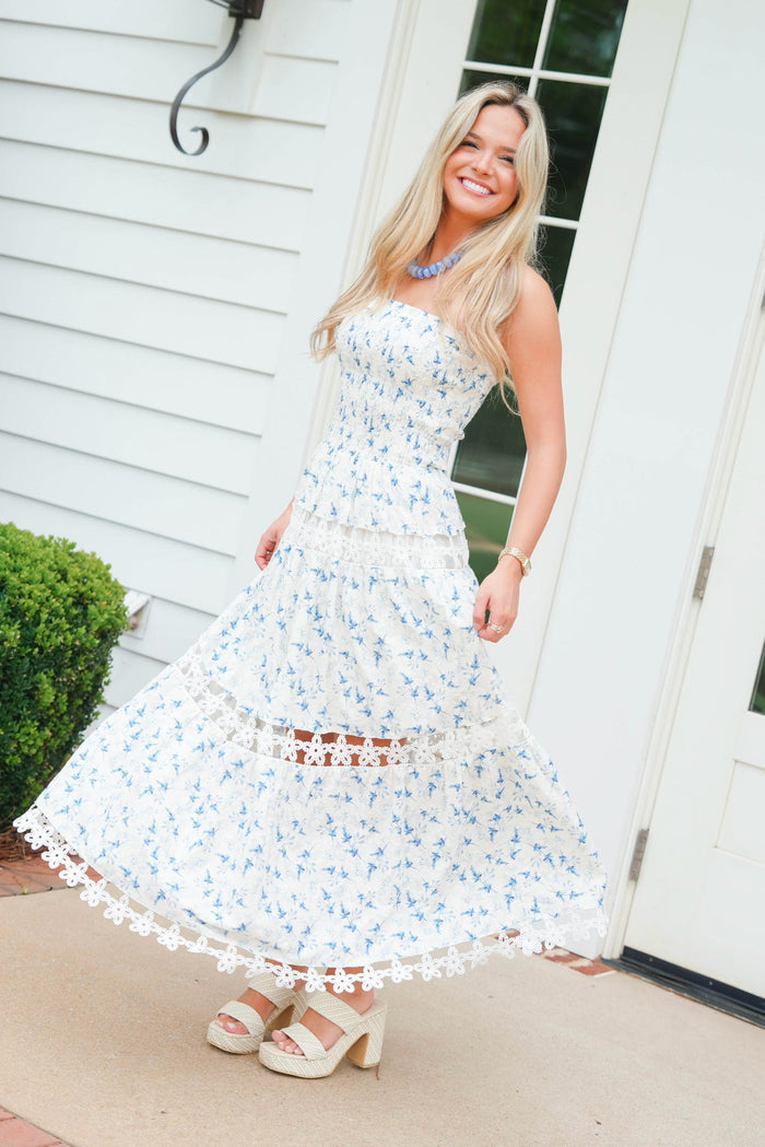 Woman wearing a floral dress standing outside a house.