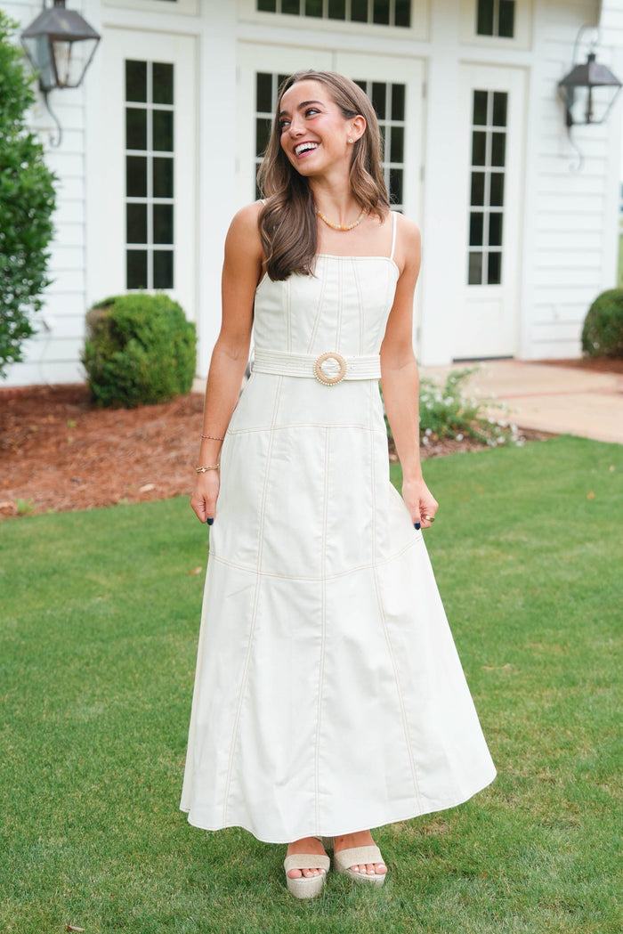 Woman in a white dress standing on grass in front of a white house.