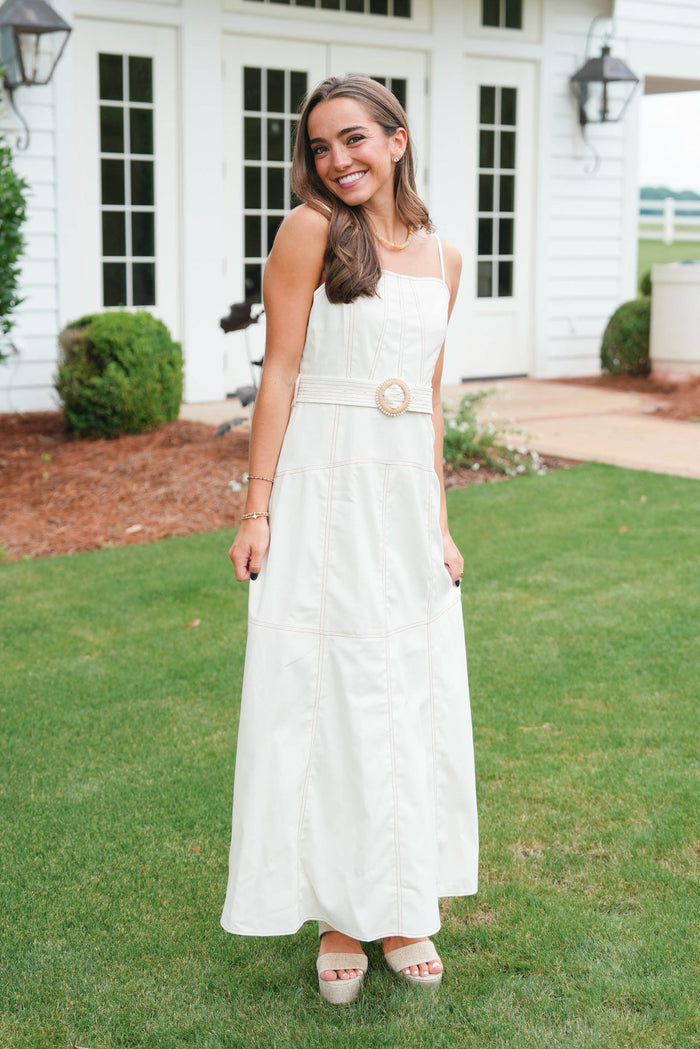 Woman in a white dress standing on grass with a white house in the background