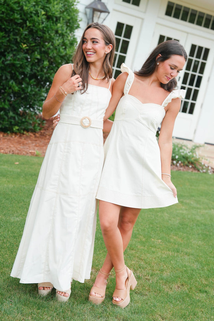 Two women in white dresses standing on grass with a building in the background