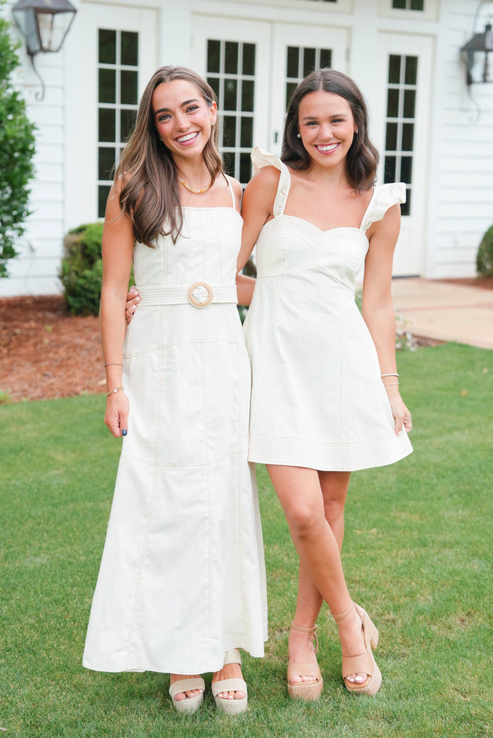 Two women in white dresses standing on grass in front of a house.