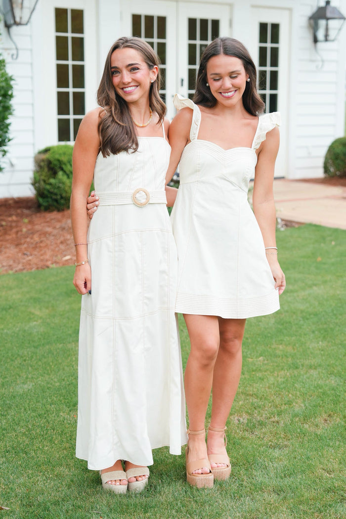 Two women in white dresses standing on grass in front of a house.