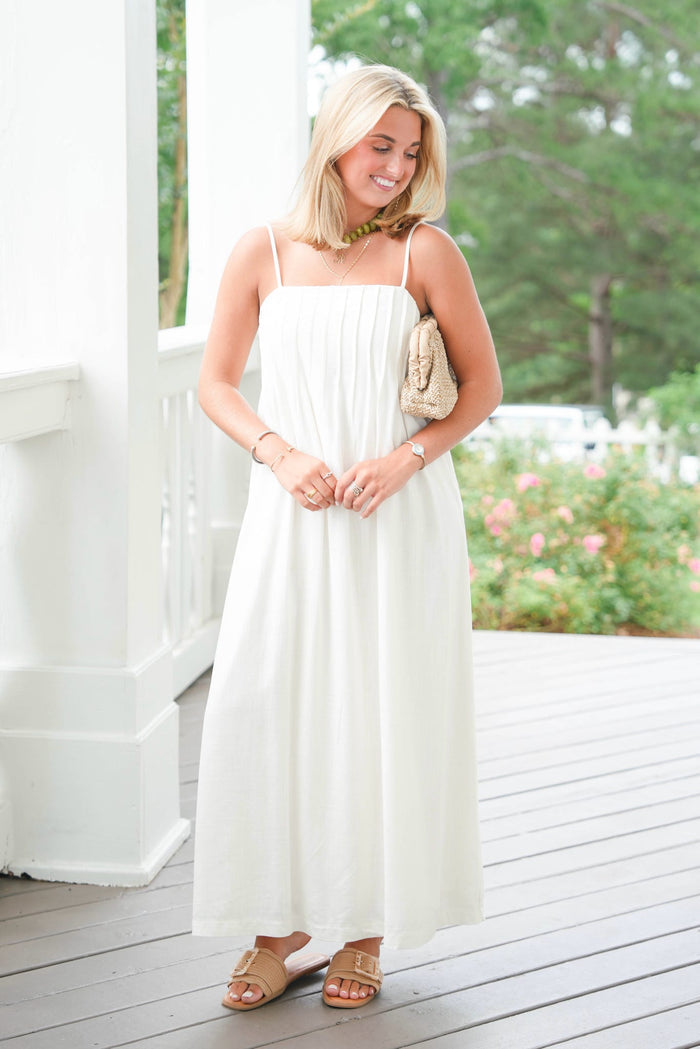 Woman in a white dress standing on a wooden deck with greenery in the background