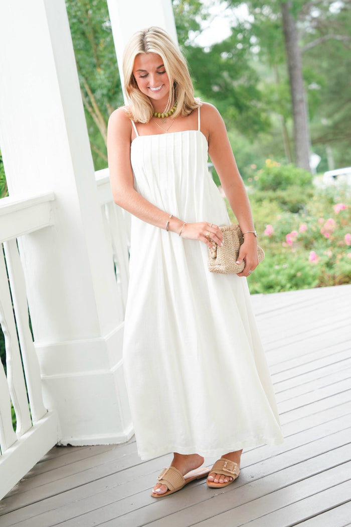 Woman in a white dress standing on a wooden deck with greenery in the background