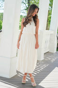 Woman in a white dress standing on a wooden deck with white columns.