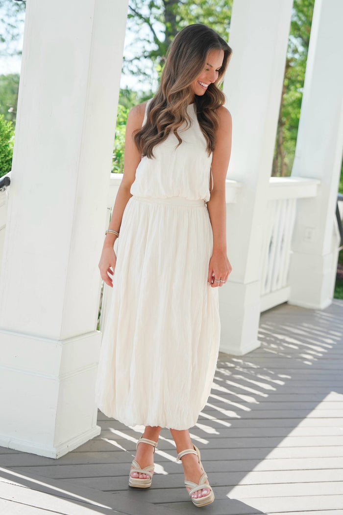 Woman in a white dress standing on a wooden deck with white columns.