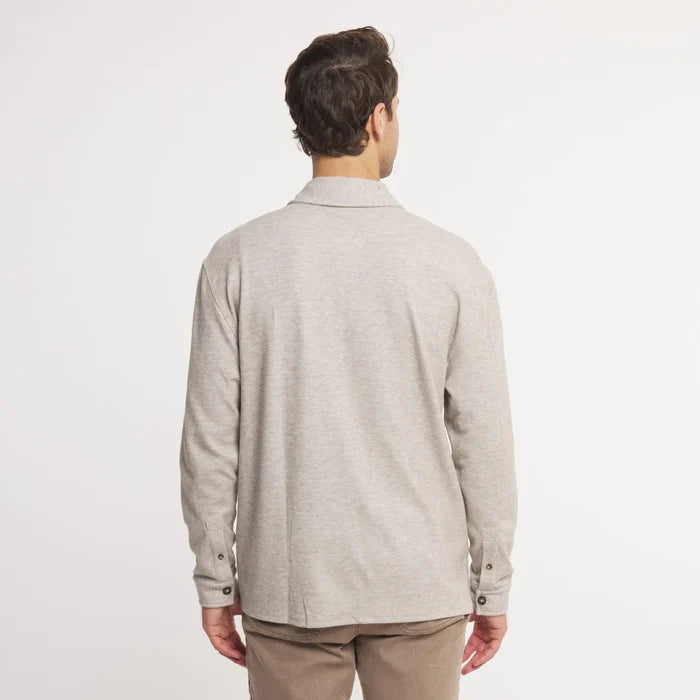 A man viewed from the back wearing a light heather gray long-sleeve knit polo shirt and tan trousers, set against a plain white studio background.