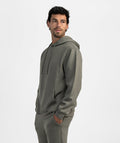 A man wearing a matching gray hoodie and sweatpants set, shown from a side profile against a clean light gray studio background.