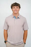 A smiling man wearing a short-sleeve polo shirt with fine horizontal stripes in beige and light blue, paired with khaki pants, photographed against a plain light gray background.