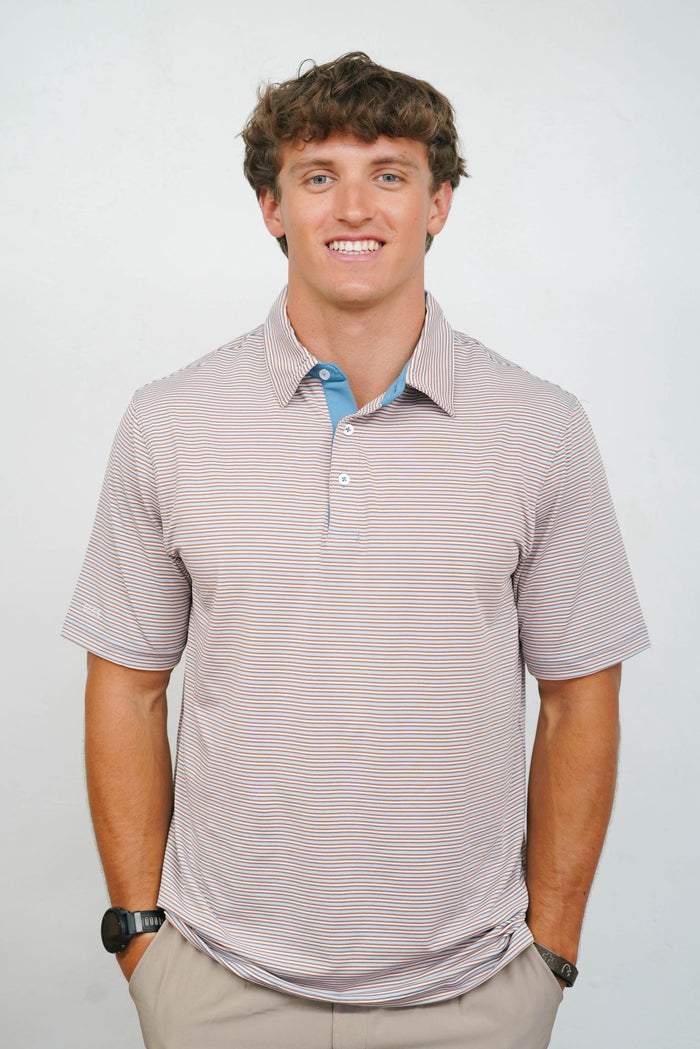 A smiling man wearing a short-sleeve polo shirt with fine horizontal stripes in beige and light blue, paired with khaki pants, photographed against a plain light gray background.
