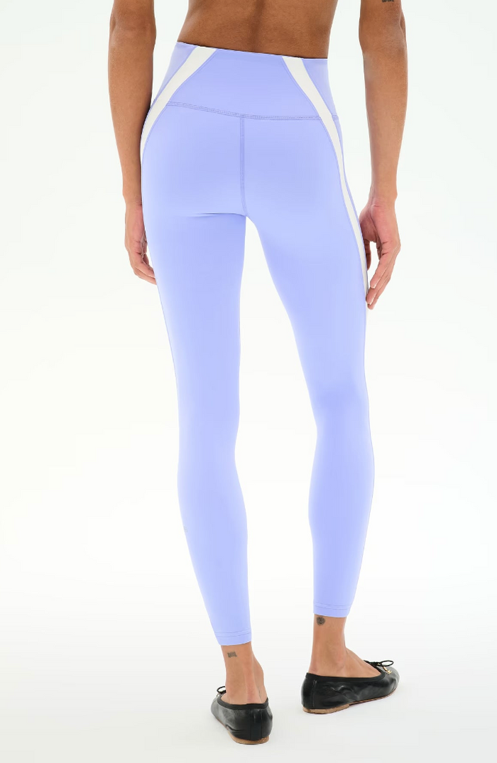 A model from the back wearing light purple high-waisted leggings with white side panels, paired with black flats, against a plain white background.