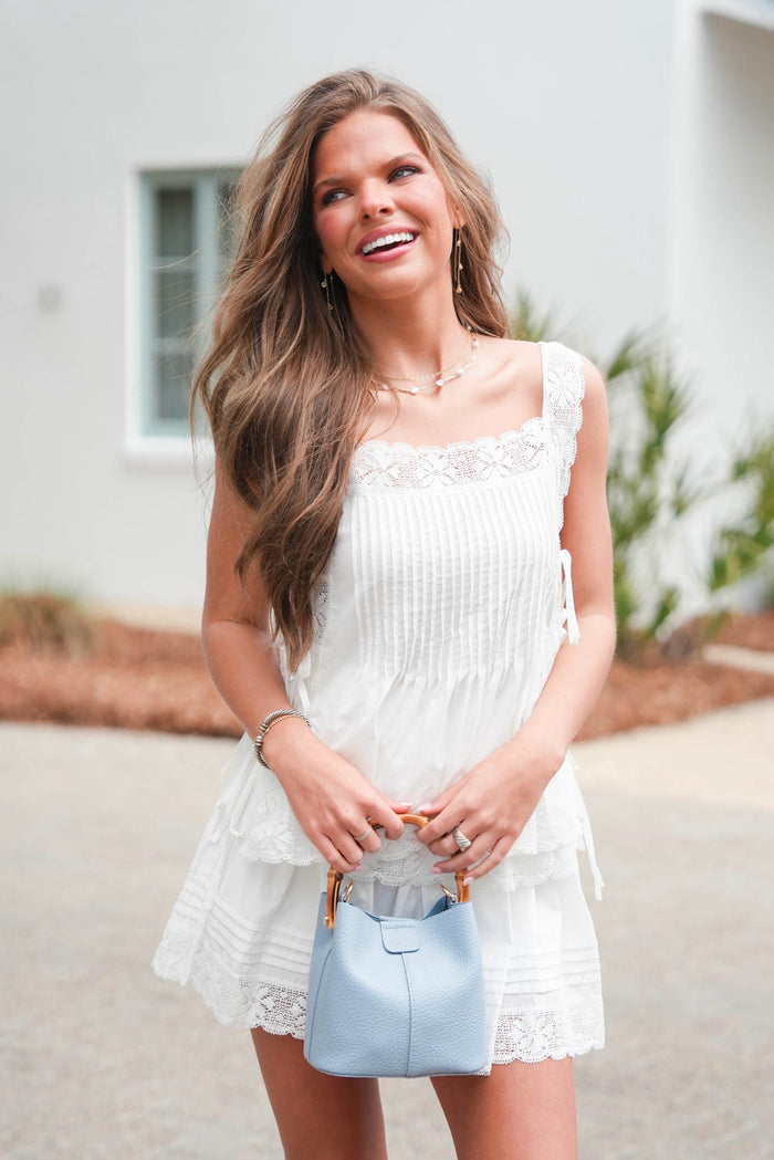 Woman in a white dress holding a light blue handbag outdoors.