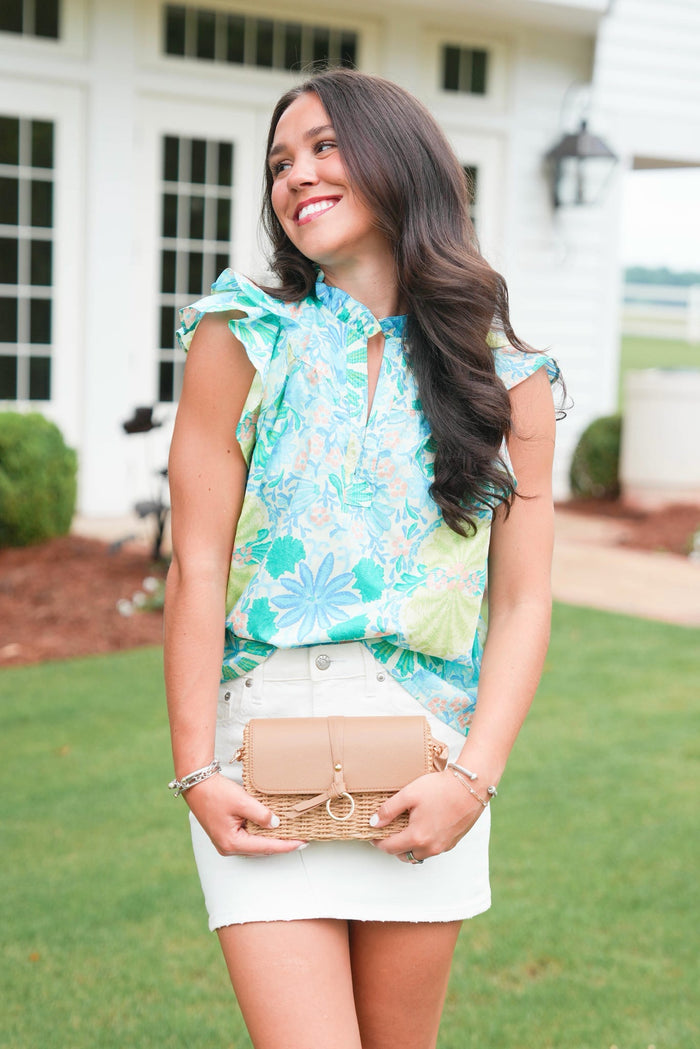 Woman in a floral top and skirt holding a woven handbag outdoors.