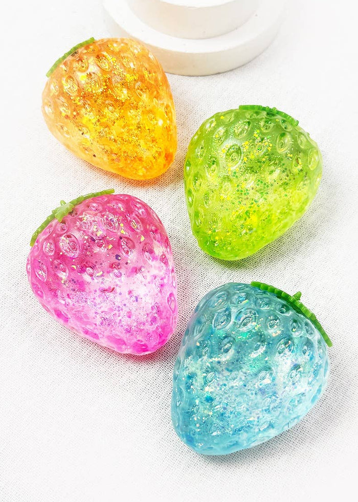 Four translucent, glittery strawberry-shaped items in yellow, green, pink, and blue, arranged on a white textured fabric surface.
