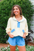 Woman wearing a yellow sweater with blue accents and blue shorts standing outdoors.