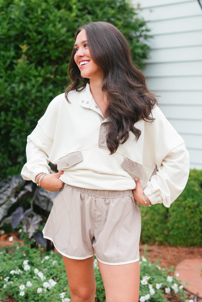 Woman wearing a beige outfit standing outdoors with greenery in the background